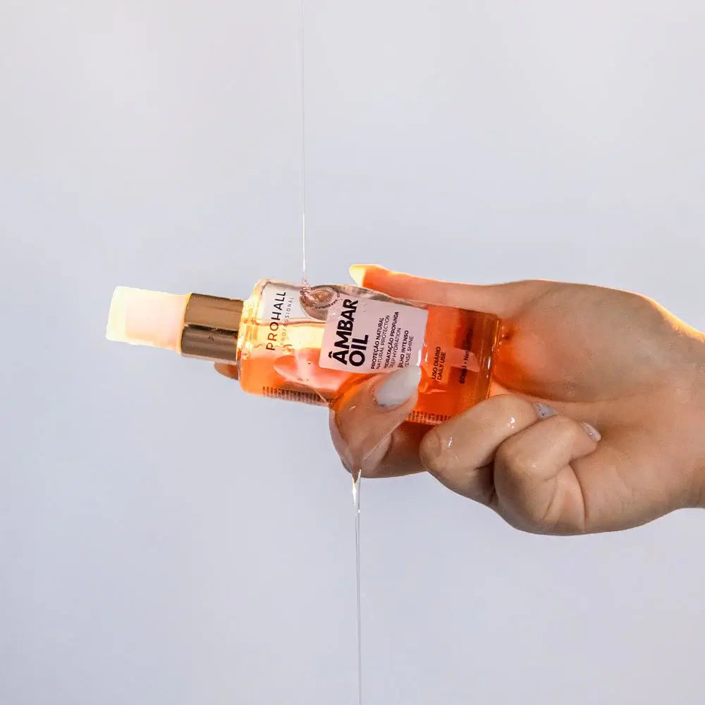 Hand holding a bottle of ambar oil with a light gray background