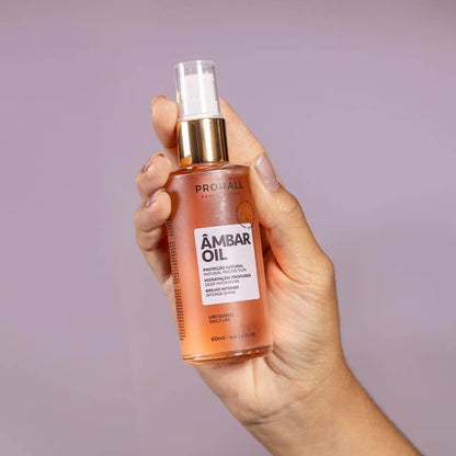 Hand holding a bottle of ProAll Ambar Oil against a purple background