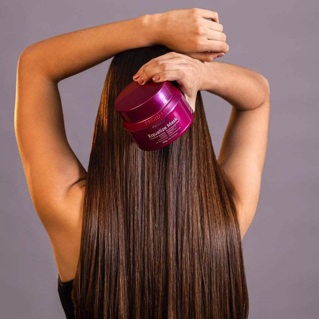 Person applying equalize hair mask product from prohall to long, straight hair against a gray background