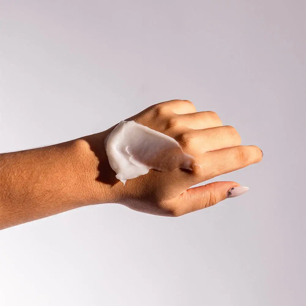 Hand applying a white cream or lotion on a plain background