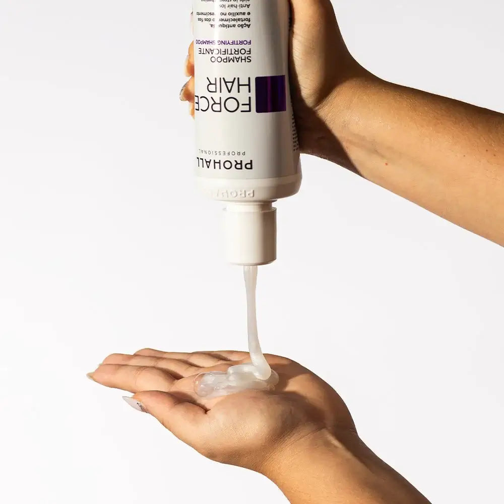 Hand holding a bottle of Prohall Force Hair product with white cream being dispensed onto another hand.