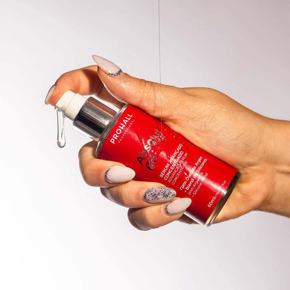 Hand holding a red bottle with a pump, against a light gray background