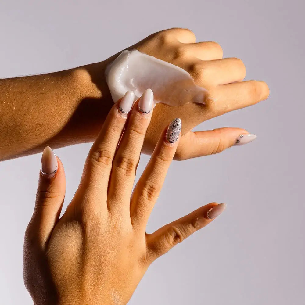 Hand applying cream to another hand against a neutral background