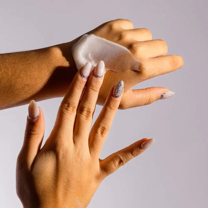 Hand applying cream to another hand against a neutral background