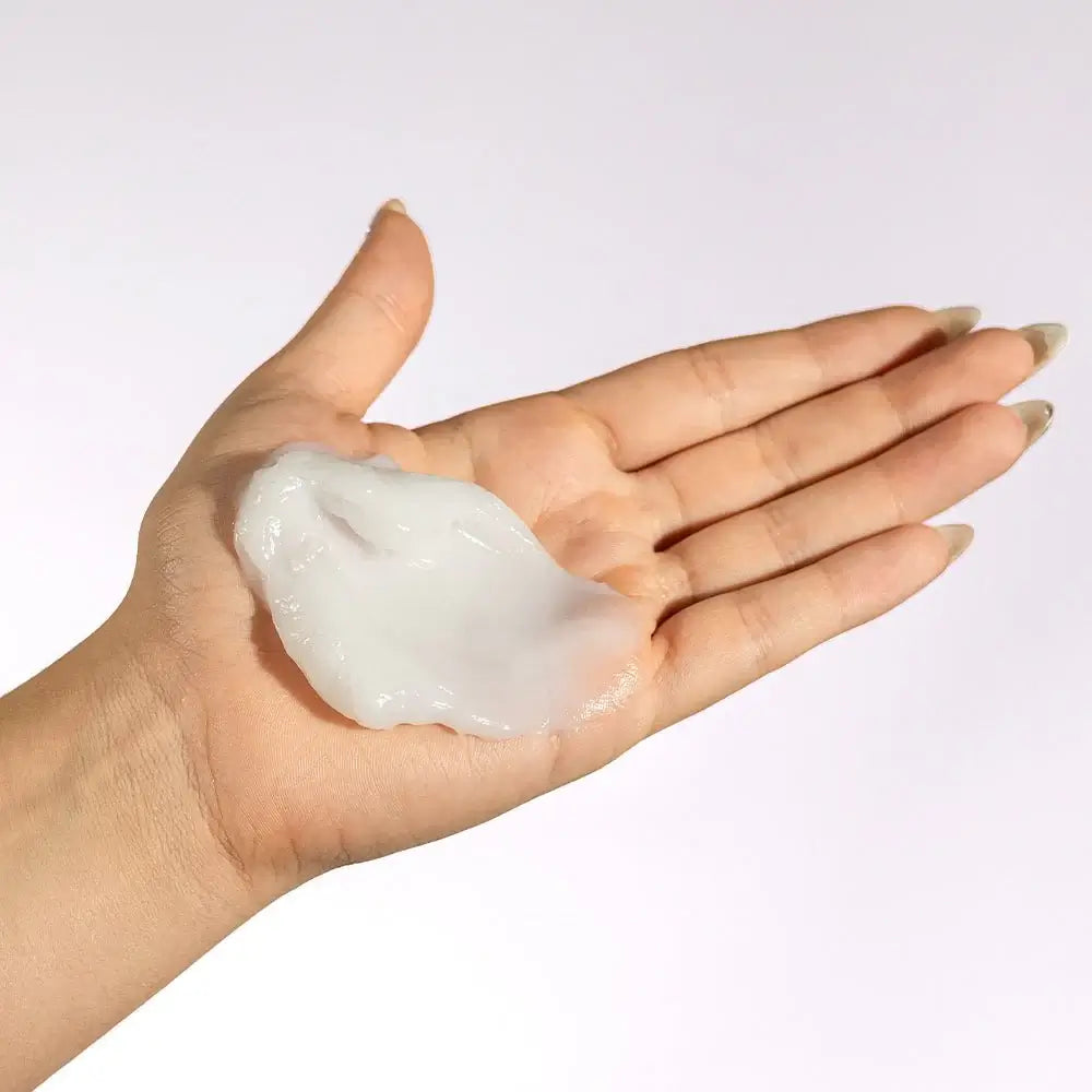 Hand holding a small amount of white cream against a light background