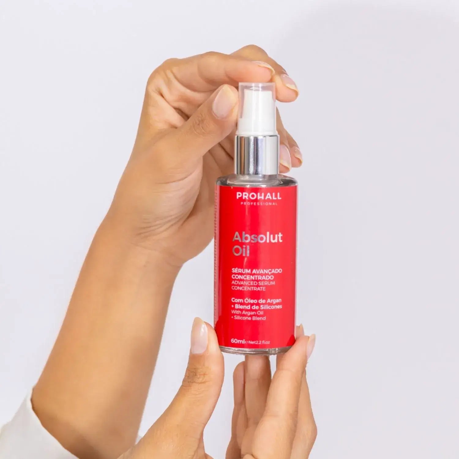 Hand holding a red serum bottle labeled 'Absolut Oil' against a light gray background