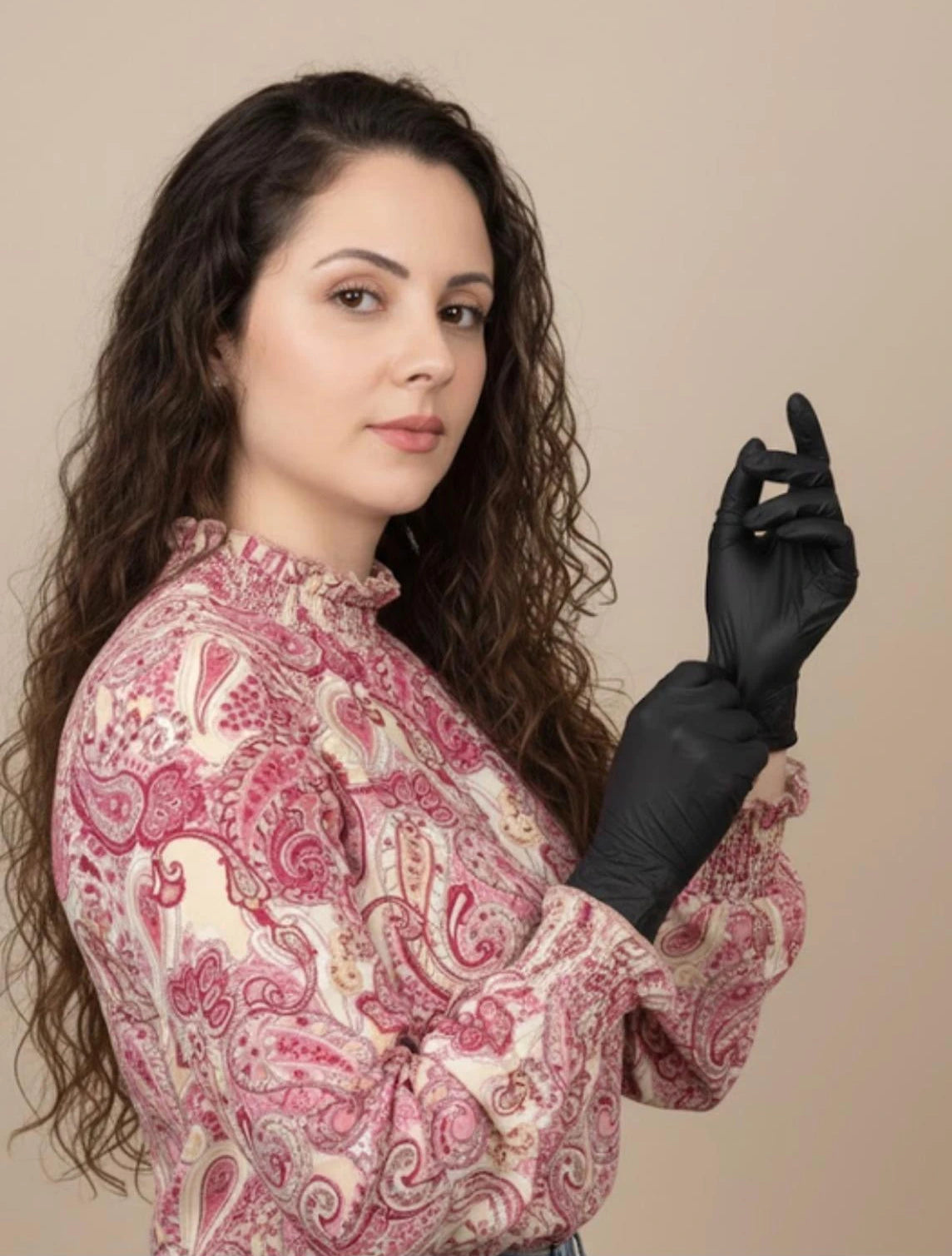 Woman wearing a patterned blouse and black gloves against a beige background